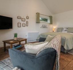 A bedroom with a bed, an armchair with pillows and a blanket, a coffee table, a wall-mounted TV, and framed pictures on the wall at Fern in Bydown near Barnstaple