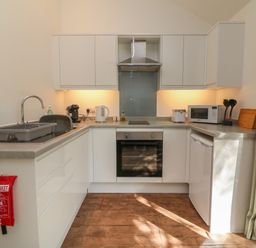 A kitchen with white cabinets a sink an oven a microwave and kitchen utensils at Fern Bydown near Barnstaple