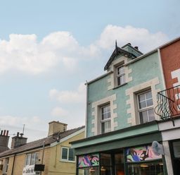 A row of colorful attached buildings with shopfronts and windows under a cloudy sky at The Bell Apartment in Cemaes Bay