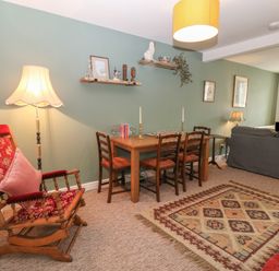A living room with a rocking chair dining table with chairs wooden shelves and a sofa at The Bell Apartment in Cemaes Bay