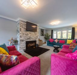 A living room with pink and teal sofas colorful pillows a fireplace and a wall-mounted TV at Parc Y Deri in Rhos-y-garth near Aberystwyth