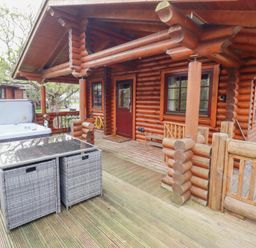 A wooden log cabin exterior with a hot tub and outdoor furniture on a wooden deck at 24 Lakeside Drive in Felton