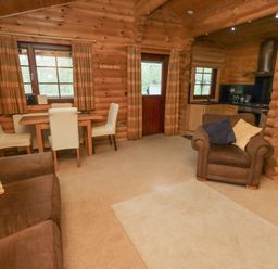 A living area with a brown sofa and armchair next to a wooden dining table with four white chairs and a small kitchen with wooden cabinets at 24 Lakeside Drive in Felton