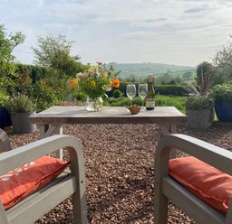 A garden with a table, chairs, flowers, and views at Church Farm Dairy Cadbury near Thorverton