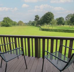 A balcony with two metal chairs overlooking a green lawn and trees at Swan in Shobdon