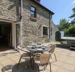 An outdoor patio with a table and chairs and a hot tub at Felin Gogoyan in Tregaron