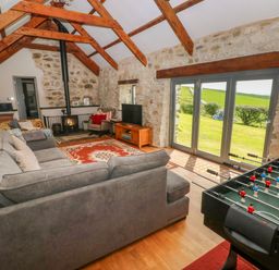 A living room with a grey sectional sofa a wood stove a foosball table and glass doors opening to a garden at Bryn Nante in Morvil near Maenclochog