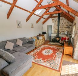 A living room with exposed wooden beams stone walls a wood burning stove a gray sectional sofa an orange patterned rug and framed animal pictures on the wall at Bryn Nante Morvil near Maenclochog