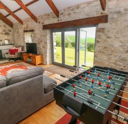 A living room with a foosball table near glass doors and a wood burning stove at Bryn Nante in Morvil near Maenclochog