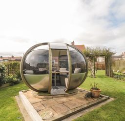 A garden with a round glass pod containing seating and a table at Coast Cottage in Bamburgh