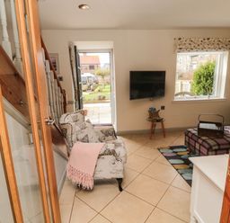 A living room with armchair near stairs wall mounted tv and window at Coast Cottage in Bamburgh