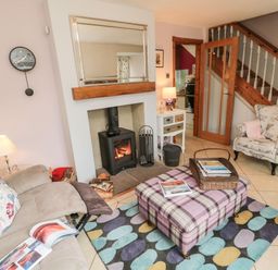 A living room with a fireplace sofa armchair ottoman rug and staircase at Coast Cottage in Bamburgh