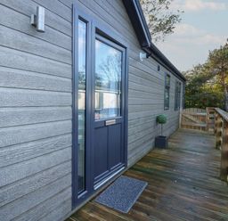 A wooden exterior deck with a dark framed glass door and a small plant at the side of a house at Lake View Lodge in Tallington
