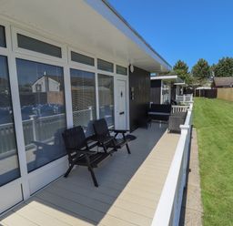 A porch with outdoor chairs and a green lawn beside it at 114 Cherry Park in Chapel St Leonards
