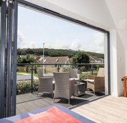 A seating area with wicker chairs and a glass table on a balcony outside a living room at Pebble Ridge View in Westward Ho
