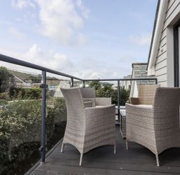 An outdoor balcony with four wicker chairs and a glass railing overlooking houses at Pebble Ridge View in Westward Ho
