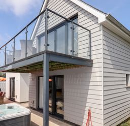 Exterior of a two-story house with a glass balcony seating area a hot tub on the patio and outdoor dining table at Pebble Ridge View in Westward Ho