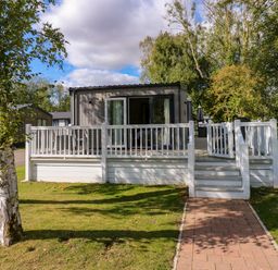 A small house with a white wooden deck and railing surrounded by grass and trees at 18 Woodlands Retreat in Tattershall