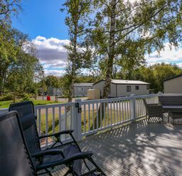 An outdoor deck with chairs and a table overlooking a residential area with trees at 18 Woodlands Retreat in Tattershall