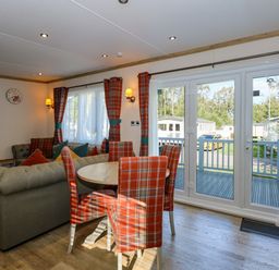 A living room with a round dining table and plaid chairs near large glass doors at 18 Woodlands Retreat in Tattershall