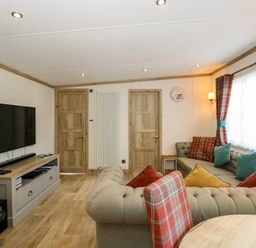 A living room with a large sectional sofa with cushions a wall mounted television wooden doors and a table at 18 Woodlands Retreat in Tattershall