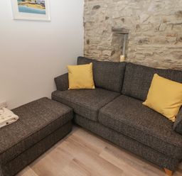 A gray sofa with two yellow cushions and a matching ottoman with a blanket in a room with a stone wall at The Nest in Amroth