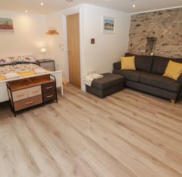 A bedroom with a bed a sofa ottoman and a stone wall at The Nest in Amroth