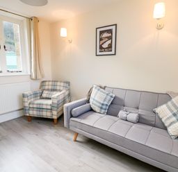A small sitting room with a grey sofa and plaid armchair near a window at Railway Station Cottage in New Radnor near Kington