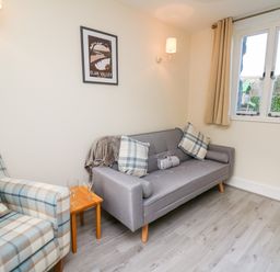 A sitting area with a gray sofa, a plaid armchair, a small wooden table with two glasses, and a window at Railway Station Cottage in New Radnor near Kington