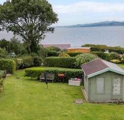 A garden with a small shed a bench and a barbecue overlooking the sea at 3 Moranedd in Moelfre