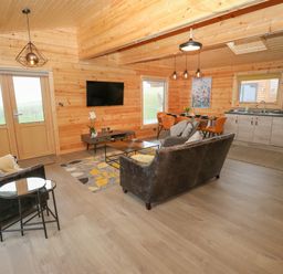 A living room with wooden walls a television a sofa and chairs a dining table and kitchen at Height End Farm Log Cabin Rossendale near Bacup