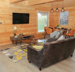 A living area with a wall-mounted TV a coffee table and seating next to a dining table with orange chairs at Height End Farm Log Cabin Rossendale near Bacup