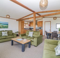 A living room with green sofas, a wooden coffee table, and a dining table with chairs at Three Views Lodge in Whitsand Bay Fort Holiday Village