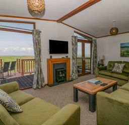 A living room with green sofas a wooden coffee table a mounted television and a fireplace at Three Views Lodge in Whitsand Bay Fort Holiday Village