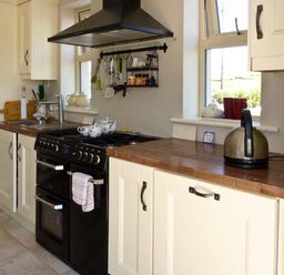 A kitchen with cream cabinets a black stove wooden countertops and windows at Bluebell Cottage in Spanish Point County Clare