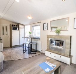 A living area with a fireplace a mirror above it a wooden coffee table and a small dining table with chairs at Hazell Thorne Hideaway in Fritton