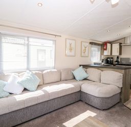 A living room with a sectional sofa and cushions next to a kitchen area with cabinets and appliances at Hazell Thorne Hideaway in Fritton