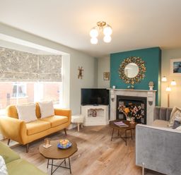 A living room with a yellow sofa a grey sofa a green chair a fireplace with a round mirror and a television at Bay Cottage in Weymouth