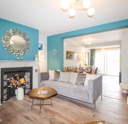 A living room with a gray sofa and a fireplace with a round mirror and flowers at Bay Cottage in Weymouth