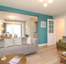 A living room with grey and green sofas a coffee table and a view into a dining area at Bay Cottage in Weymouth