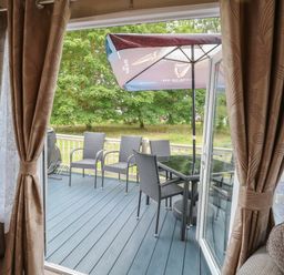 A patio with four chairs a table and an umbrella visible through open doors with curtains at Stanley's Lodge Foxburrow Hang Belton Norfolk