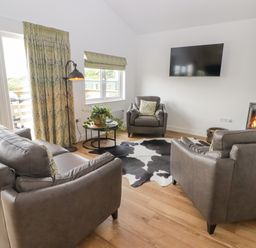 A living room with leather sofas a round table with plant a wood burning stove and a wall mounted television at Monks Rest in Monknash