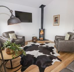 A living room with two leather chairs a wood burning stove a wall mounted television and a cowhide rug at Monks Rest in Monknash
