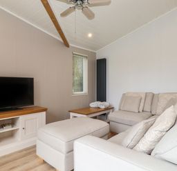 A living room with a television on a wooden cabinet a beige sofa and ottoman a wooden coffee table and a ceiling fan at Serendipity R11 Fallbarrow Park near Bowness-On-Windermere