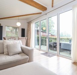 A living room with beige sofas, large glass sliding doors leading to a patio and dining area at Serendipity in R11 Fallbarrow Park near Bowness-On-Windermere