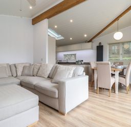 A living room with beige sectional sofa and ottoman next to a dining area with table and chairs at Serendipity R11 Fallbarrow Park near Bowness-On-Windermere