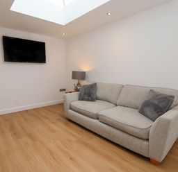 A room with a gray sofa two gray cushions a lamp a wall mounted television and wooden flooring at The Woodpecker in Scarborough
