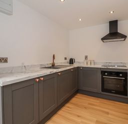 A kitchen with grey cabinets a marble countertop an oven a stovetop and a sink at The Woodpecker in Scarborough