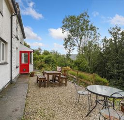 An outdoor patio area with wooden picnic table and benches a round glass table with metal chairs and a red door on a white building at Delfryn in Goginan near Aberystwyth