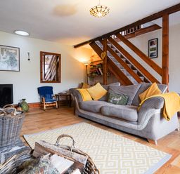 A living room with a gray sofa yellow cushions a wooden staircase and baskets with firewood at Delfryn Goginan in Goginan near Aberystwyth